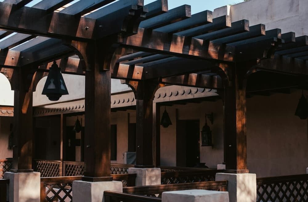 Pergola en bois sombre adossée à une maison au-dessus d’un coin repas