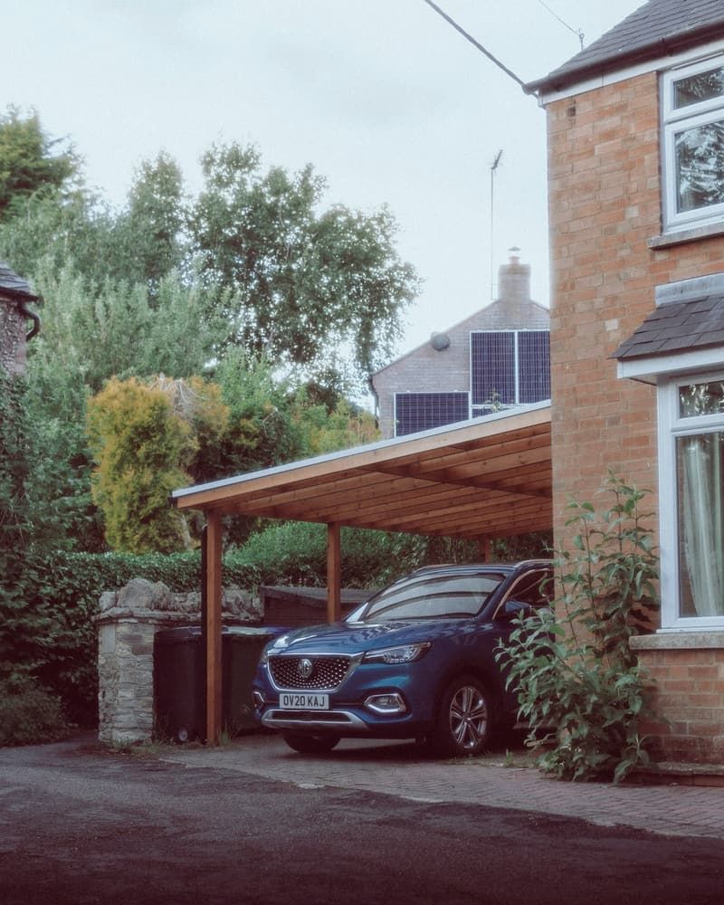 Voiture garée sous un carport en bois accolé à une maison